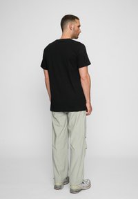 Sort bomulds t-shirt med korte ærmer, parret med lysegrå cargo bukser. Har en afslappet pasform og standard rund halsudskæring.