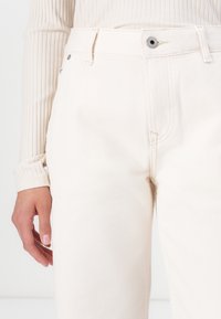 Lys beige jeans med en rett snitt, laget av denimstoff. Har en metallknapp, synlige sømmer og detalj med sidelomme.