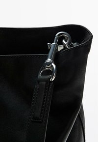 Zwarte leren handtas met een gestructureerd oppervlak, zilverkleurige handgrepen, een kliksluiting en een zachte, ongestructureerde vorm.