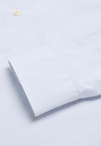 Camisa de algodón a cuadros azul claro con cuello abotonado y mangas largas. La tela presenta un patrón de cuadrícula fina y una textura suave.
