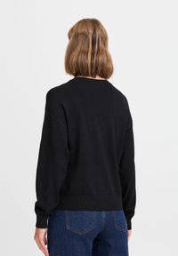 Maglione nero con maniche lunghe e scollo rotondo, con orlo e polsini a coste, realizzato in tessuto morbido e strutturato.