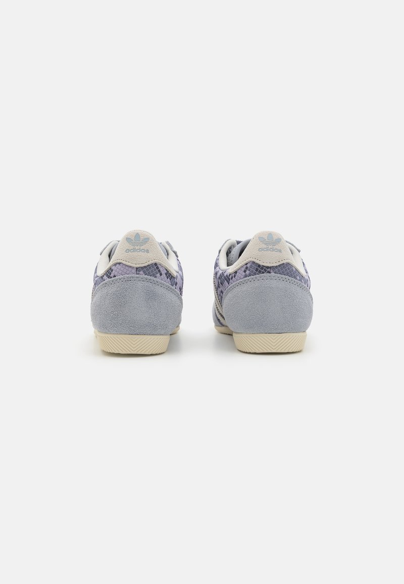 Sneaker in suede grigio con tomaia in rete decorata, dotate di una suola in gomma color crema e un logo blu chiaro sul tallone.