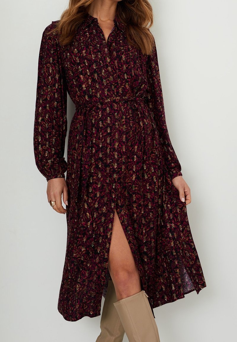 Långärmad burgundröd klänning med blommönster, krage och framficka, åtdragen vid midjan, tillsammans med tan knähöga stövlar.