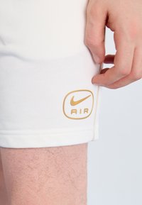 White athletic shorts with a smooth texture, featuring a gold Nike "AIR" logo on the lower left side near the hem.