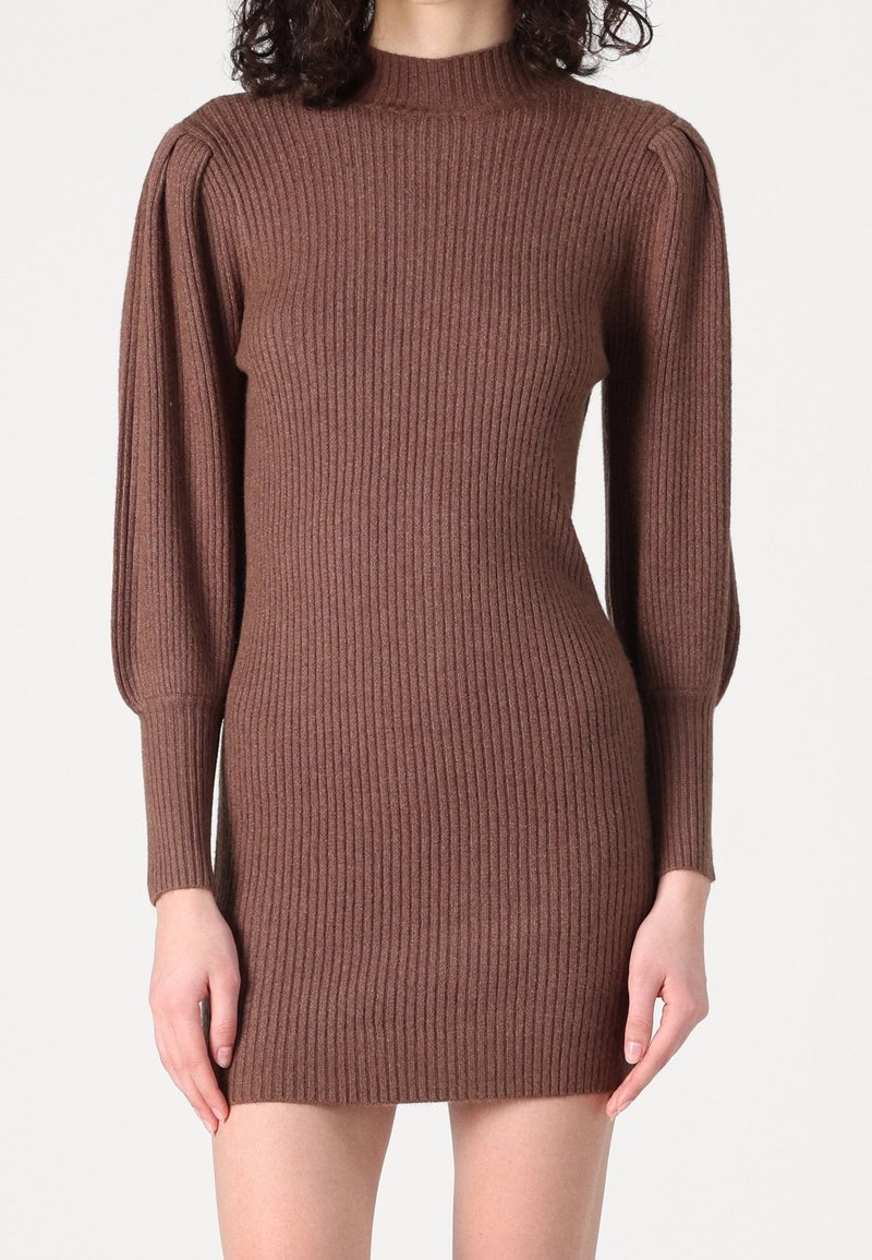 Femme portant une robe-pull en maille côtelée marron avec de longues manches ballon et un col montant, visible des épaules jusqu'à mi-cuisse.