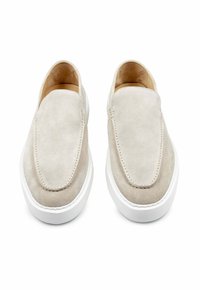 Beige suede instappers met een ronde neus, witte rubberen zool en subtiele stiksels op het bovenoppervlak. Zachte binnenvoering.