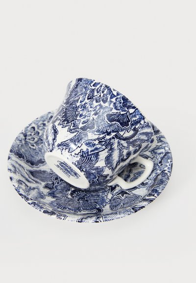 Ceramic teacup and saucer set in blue and white floral pattern, with a curved cup shape and a handle, resting on a decorative saucer.