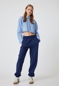 Korte blauwe gestreepte blouse met lange mouwen en kraag, gecombineerd met marineblauwe joggers met een elastische tailleband en taps toelopende boorden.