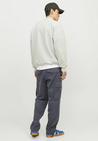 Lysegrå sweatshirt med ribbede manchetter, parret med mørkegrå cargo-bukser med sidelommer. Blå sneakers med brune såler fuldender outfittet.