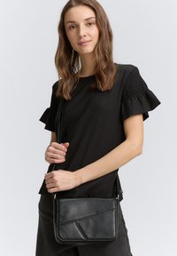 Schwarze Leder-Crossbody-Tasche mit geometrischem Design, Reißverschluss, verstellbarem Tragegurt und geprägtem Logo. Glatte Textur und kompakte Form.
