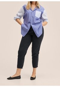 Camisa de botones a rayas azul y blanca con un bolsillo liso, combinada con pantalones vaqueros cortos negros y planos negros. Textura suave, ajuste relajado.