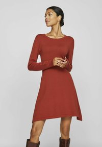 Robe longue manches longues bordeaux avec un col rond et un ourlet asymétrique. Fabriquée dans un tissu doux et texturé, ajustée au niveau du corsage et fluide au niveau de la jupe.
