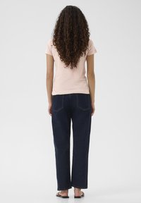 Pink cotton t-shirt and dark blue, straight-leg jeans with two back pockets. Model wears black sandals; hair is curly and long.