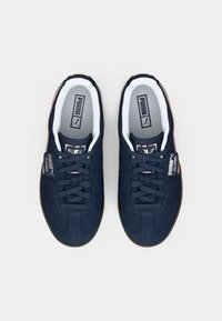 Navy suede sneakers with a rounded toe, lace-up design, white interior lining, and a gum rubber sole. Features "PUMA" logo detail.