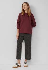 Bordeaux hoodie met trekkoorden, gecombineerd met geweven zwarte cropped broeken en witte sneakers met bruine accenten.
