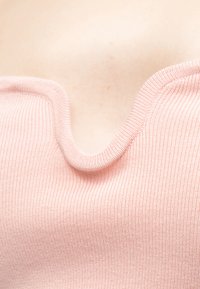 Κοντινό πλάνο ενός ροζ ανοιχτού ριμπ πλεκτού ρούχου με βαθύ, κυματιστό ντεκολτέ που αποκαλύπτε ι ανοιχτόχρωμο δέρμα από πάνω.