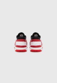 Urheilukengät, joissa musta päällinen, valkoinen välikenkä ja punaiset yksityiskohdat. Kuvioitu kumipohja erottuvalla kulutuspohjalla.