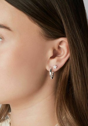 Sølv hoop øreringe med tekstureret detalje og en lille stjernesstud, båret af en model, der tydeligt viser design og tekstur.