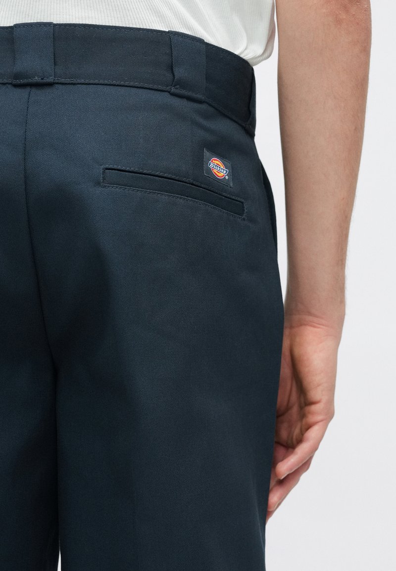 Dunkelblaue Hose mit glatter Textur, ausgestattet mit einer aufgenähten Tasche und einem Markenschild auf der Rückseite. Gerades Schnitt-Design.