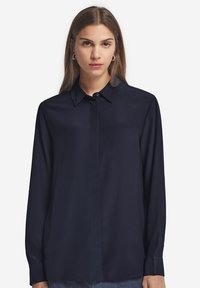 Granatowa koszula z długim rękawem, z kołnierzykiem zapinanym na guziki, wykonana z gładkiego materiału, z zapięciem z przodu i luźnym krojem.