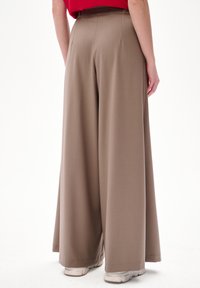 Szerokie spodnie w gładkim, beżowym materiale. Posiadają wysoki stan i starannie wykończone szwy, zestawione z białymi trampkami na dole.