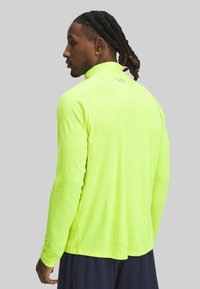 Langermige sportshirt in felneon geel, met een hoge kraag en gladde, textuurstof. Logo op de rug nabij de nek.