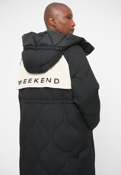 Μαύρο τζάκετ πούφφας με κουκούλα, με κρεμ χρώματος πίσω πάνελ που φέρει την επιγραφή "WEEKEND" σε μαύρο κείμενο. Υφαντό ύφασμα και oversized εφαρμογή.