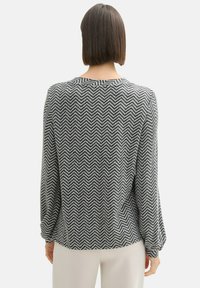 Blusa de manga larga en blanco y negro con un patrón de espiga, con cuello redondo y un corte relajado, que presenta mangas ligeramente abullonadas y una textura suave.