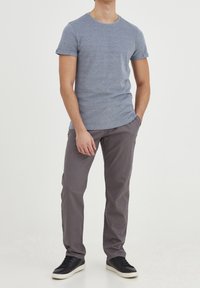 Grå kortärmad t-shirt med rund hals, kombinerad med slim-fit grå byxor och svarta sneakers. Bomullstyg, mjuk textur.