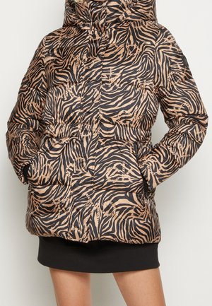 Puffer jacket with brown and black zebra stripes, hands in zippered pockets, worn over a black skirt.