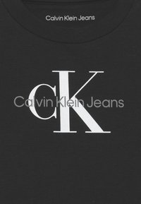 T-shirt en coton noir avec un grand logo "CK" blanc centré sur la poitrine, avec "Calvin Klein Jeans" imprimé au-dessus dans une police plus petite.