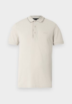 Beežist puuvillane polo-särk, millel on kaherealine nööpimine, mustad ääred krae ja varrukate piirkonnas ning rinnal tikitud logo.