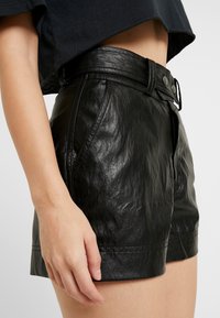 Svarta lädershorts med en strukturerad yta, hög midja, bälteshällor och framfickor. Har en slät dragkedja och knappstängning.