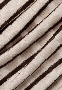 Beige und braun gestreifter Stoff mit einer strukturierten Musterung. Das Design zeigt abwechselnd rechteckige Webarten, die ein gitterähnliches Erscheinungsbild erzeugen.