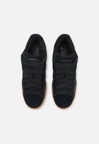 Mustat mokkasneakersit kumipohjalla, tasaisilla nauhoilla, pehmustetulla kielillä ja sivussuunnassa olevilla tehosteilla. Teksturoitu päällinen ja klassinen muotoilu.