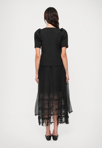 Sort kjole med korte pufærmer, der har en tætsiddende overdel og en gennemsigtig, lagdelt nederdel prydet med blomster-lace detaljer.