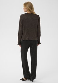 Pull marron texturé avec des accents scintillants, manches longues et ourlet à volants, associé à un pantalon noir et des chaussures noires à petit talon.