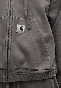 Γκρι φούτερ με φερμουάρ, μπροστινή τσέπη, κορδόνι και μικρό λογότυπο Carhartt στην πάνω περιοχή της τσέπης.