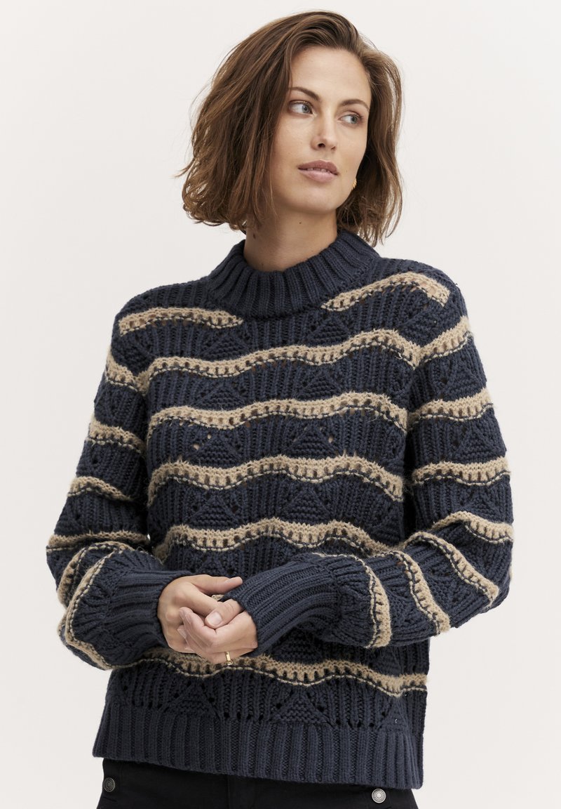 Navy gestrickter Pullover mit einem strukturierten Muster aus beigen Wellenstreifen, ausgestattet mit einem gerippten Kragen und umgeschlagenen Ärmeln. Grober Garn mit offenen Maschen.