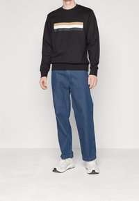 Svart sweatshirt med horisontella ränder i beige, vitt och mörkgrått. Kombineras med avslappnade blå jeans och vita sneakers.