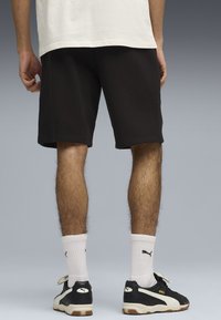 Svarta bomullsshorts med elastisk midjeband, bärs med vita strumpor och svarta sneakers. Sneakers har ett beige och svart mönster.