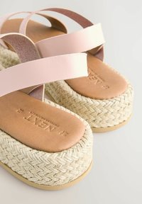 Rosa läderkorsremmar på en espadrille-sandal, med en strukturerad vävd jute-sula och en slät tan läderfotsäng med präglad märkning.