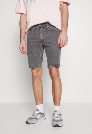 Szare szorty dżinsowe z postrzępionymi brzegami, zestawione z jasnoróżowym, oversize'owym t-shirtem. Modelka nosi jasnoszare trampki i białe skarpetki do kostek.