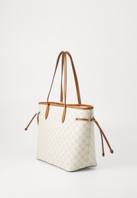 Un sac tote crème élégant avec une surface texturée, doté de poignées en cuir marron et de fermetures à cordon sur les côtés.