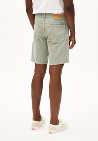 Lichtgroene cargoshorts van zachte katoen met een discreet logo-opnaaipatch aan de achterkant, twee achterzakken en een relaxte pasvorm, gecombineerd met witte sneakers.