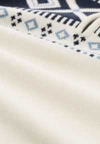 Strickstoff mit weißem Grund und blauen geometrischen Mustern. Weiche Textur mit auffälligen kontrastierenden Designs in Marineblau und Hellblau.