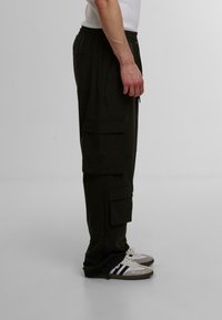 Svart cargo bukser med flere lommer, elastisk midje og en avslappet passform. Kombinert med joggesko med et svart og hvitt design.