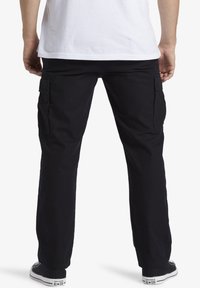 Black cargo pants with side pockets, made of sturdy fabric. Straight leg design, paired with black and white sneakers.