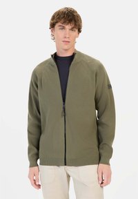 Olivengrøn zip-up sweater med ribbet tekstur, raglanærmer og fladstrikket krave, med et sort mærke på venstre arm.