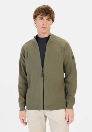 Olivengrøn zip-up sweater med ribbet tekstur, raglanærmer og fladstrikket krave, med et sort mærke på venstre arm.